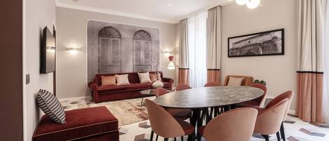 Una sala de estar moderna con un sofá rojo, una mesa redonda de comedor con sillas y un gran ventanal con cortinas.