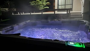 A hot tub with a digital control panel, surrounded by a wooden deck and a stone wall. - Spa & Spacious (Rotorua)