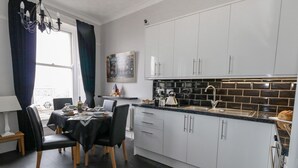 A modern kitchen with white cabinets, a black countertop, and a dining area with a table set for two. - Sunbeach (Weymouth)
