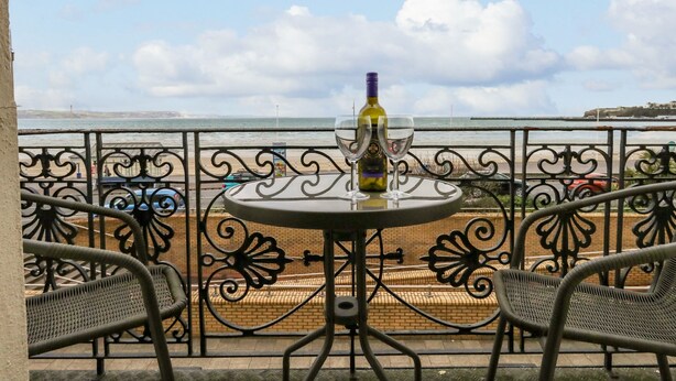 A balcony with a table, two chairs, a bottle of wine, and two glasses. The view includes a beach and the sea. - Sunbeach (Weymouth)