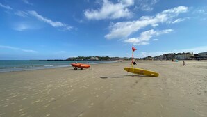 A beach with lifeguard equipment, including a red flag and a yellow surfboard, and a lifeguard boat. - Sunbeach (Weymouth)