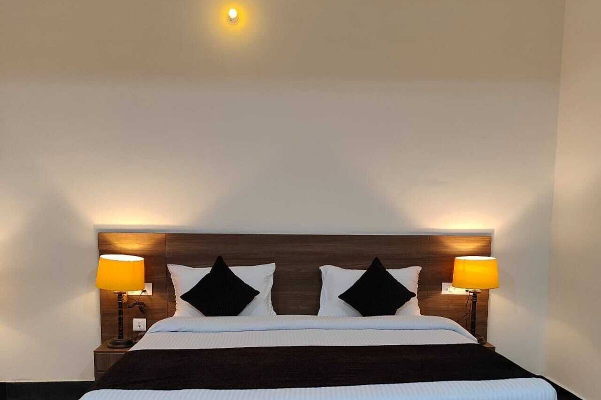A standard hotel room with a large bed, two bedside lamps, and a simple headboard.