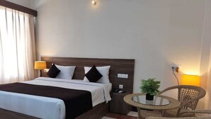 Ein Hotelzimmer mit einem großen Bett, Nachttischen, einem kleinen runden Tisch mit Stühlen und einer Topfpflanze.