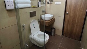 Ein Badezimmer mit Toilette, Waschbecken und Dusche. Handtücher und Pflegeprodukte hängen an der Wand.