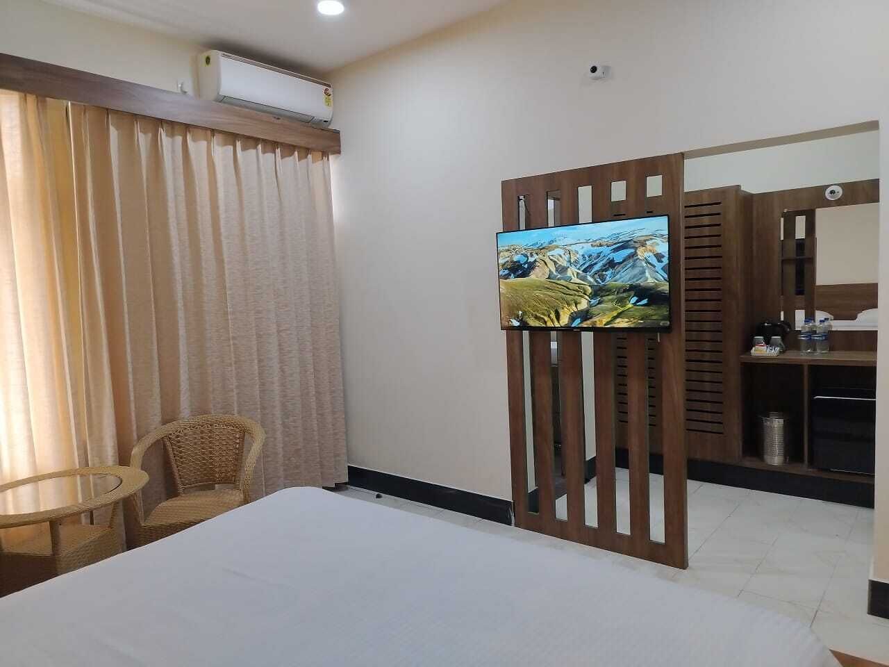 A hotel room with a bed, a TV on a wooden stand, a wicker chair, and a small table.