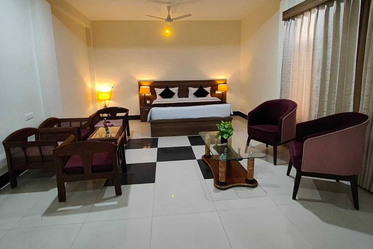 A hotel room with a bed, two bedside lamps, a ceiling fan, a checkered floor, and four chairs.