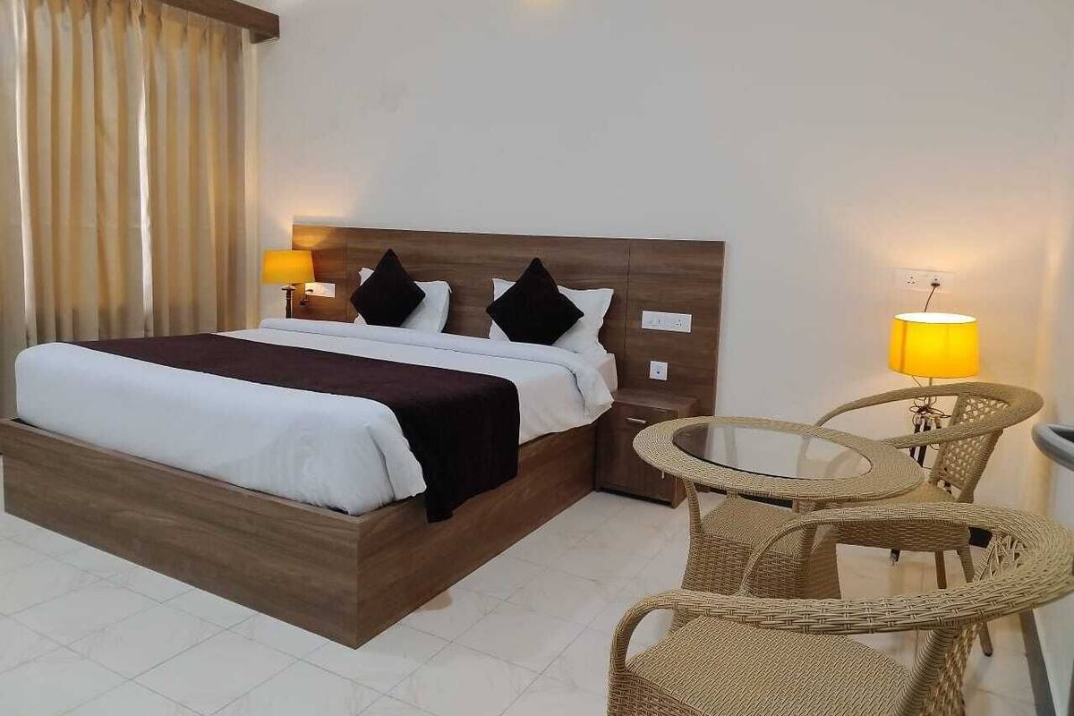 A hotel room with a wooden bed, two bedside tables, a round wicker table, and a lamp.