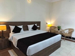 A hotel room with a large bed, two bedside lamps, a small table with a chair, and a potted plant.