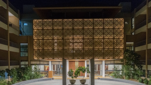 A modern building with a patterned facade, a courtyard with potted plants, and a reception area with a wooden door. - Pathikashram Nilaya (Gandhinagar)