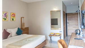 A modern hotel room with a bed, a desk with a chair, a mirror, and a shower area. - Pathikashram Nilaya (Gandhinagar)