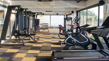 A gym with various exercise equipment, a checkered floor, and large windows offering a view of the outdoors.