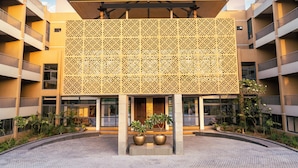 A modern building with a patterned facade, multiple balconies, and a central courtyard with potted plants. - Pathikashram Nilaya (Gandhinagar)