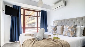 Ein modernes Hotelzimmer mit einem großen Bett, einem Flachbildfernseher und einem Fenster mit Vorhängen.