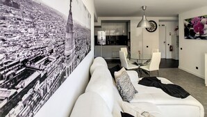 Ein modernes Wohnzimmer mit einer großen Stadtkulissen-Muralmalerei, einem Essbereich mit Glastisch und Stühlen sowie einer Küche im Hintergrund.