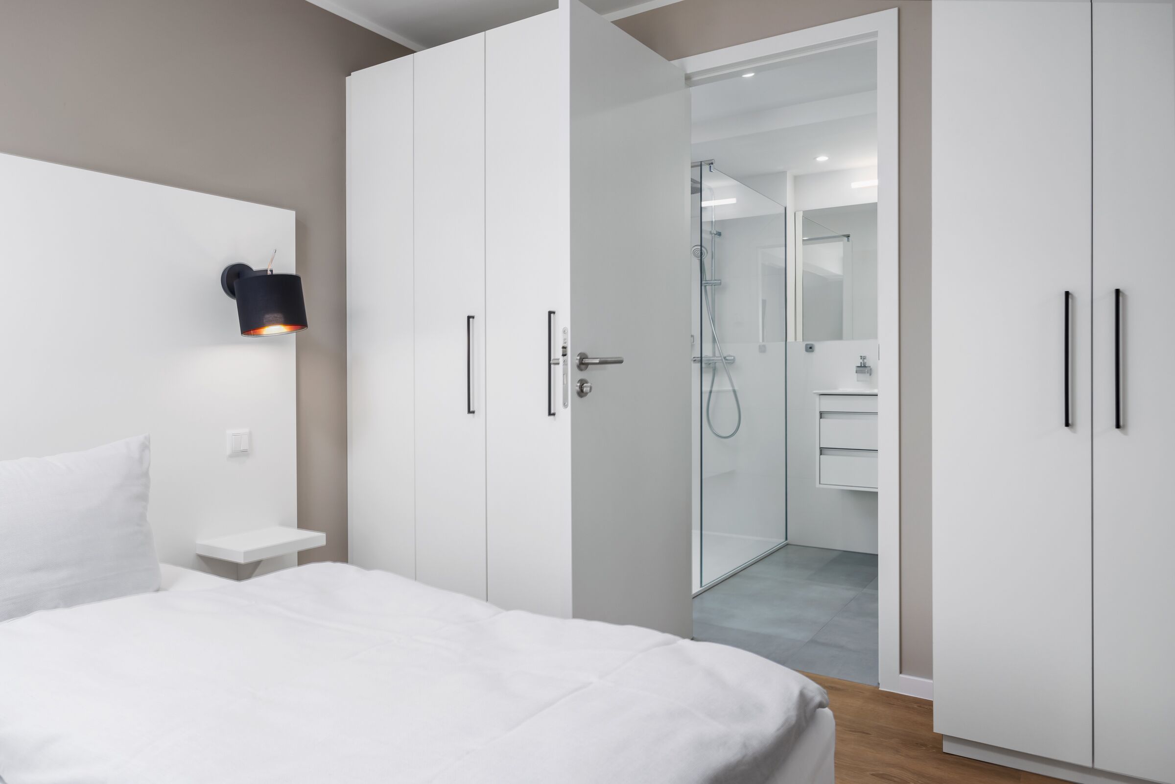 A modern bedroom with a bed, a nightstand, a wardrobe, and a bathroom visible through an open door.