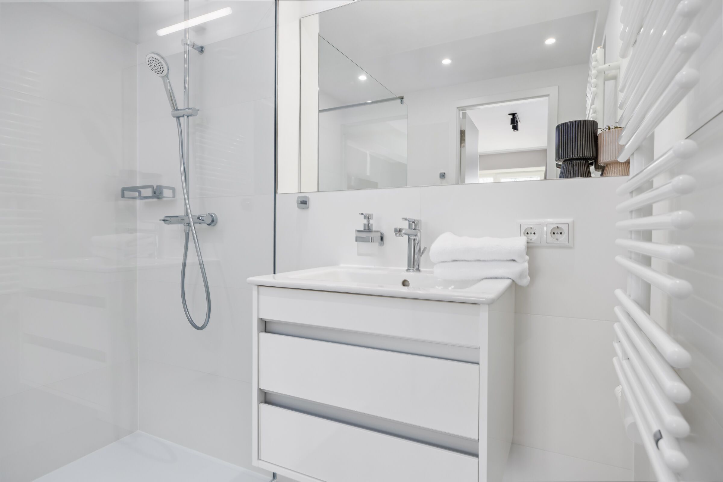 Un baño moderno con cabina de ducha de vidrio, un tocador blanco con espejo y un perchero para toallas.