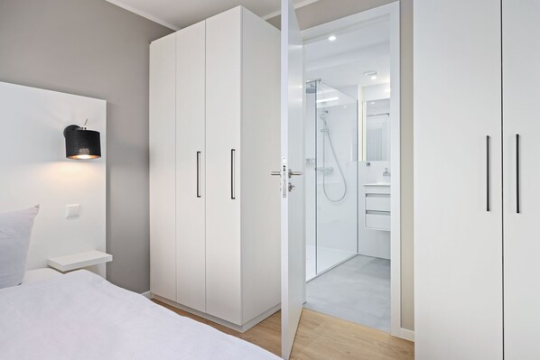 A modern bedroom with a bed, a wardrobe, and a walk-in closet leading to a bathroom with a shower and a mirror.