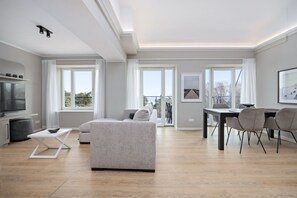 A modern living room with a sofa, a dining table with chairs, a TV, and large windows.