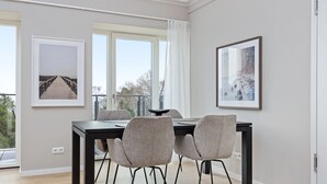 Uma sala de jantar moderna com mesa preta e quatro cadeiras cinzas, obras de arte nas paredes e janelas amplas com vista para árvores.