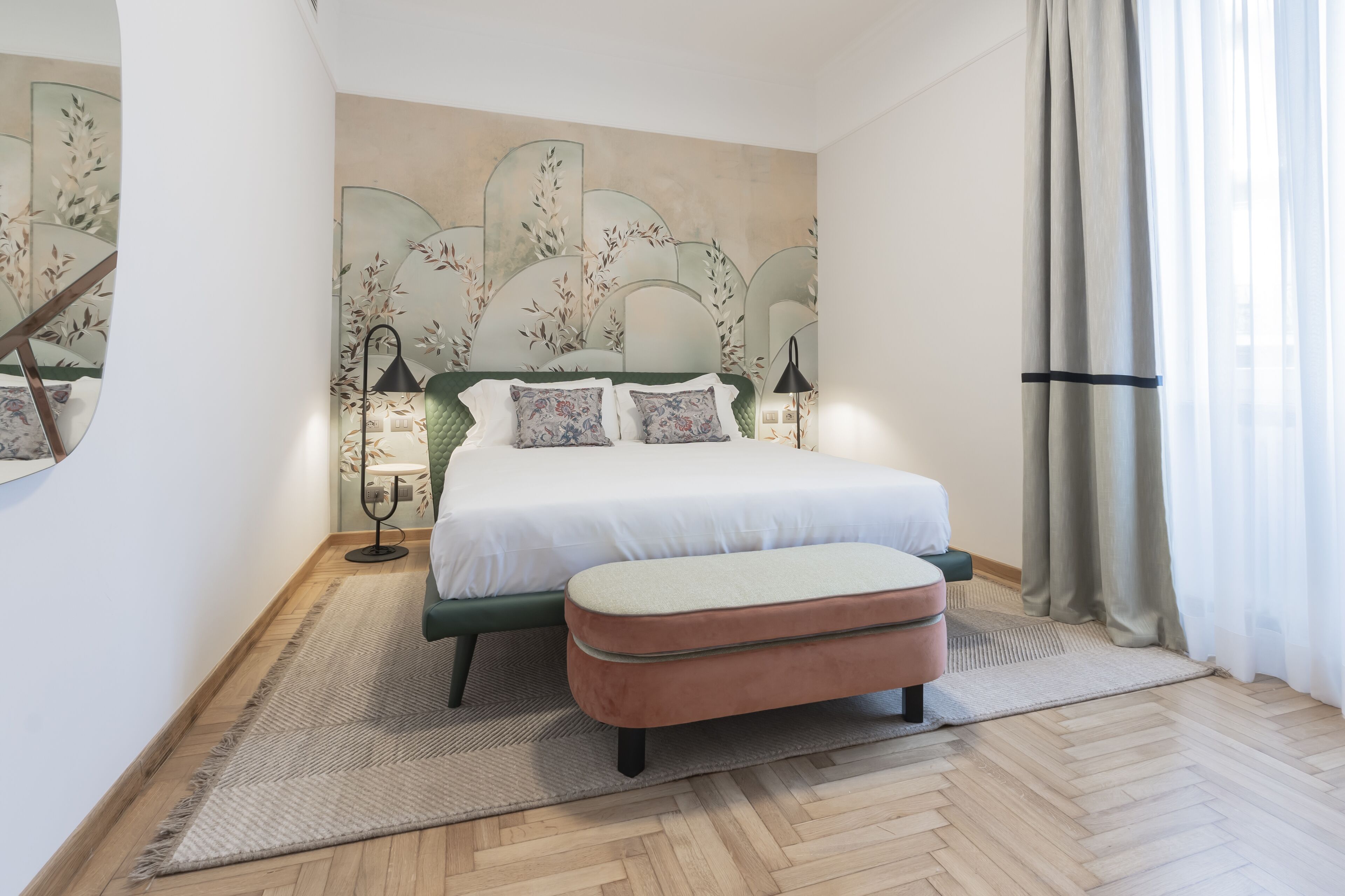 A bedroom with a bed, a bench, a lamp, and a wall with a leaf pattern.