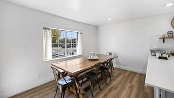 A dining area with a wooden table and chairs, a window with curtains, and a kitchen counter with utensils.