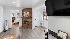 A modern living room with a fireplace, a flat-screen TV, and a welcome sign. - Happy Trails Bed and Breakfast (Tropic)