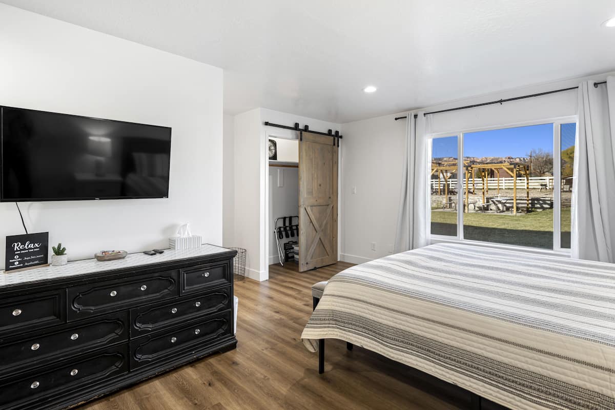 A bedroom with a large bed, a TV on the wall, a dresser, and a sliding barn door leading to an outdoor area.