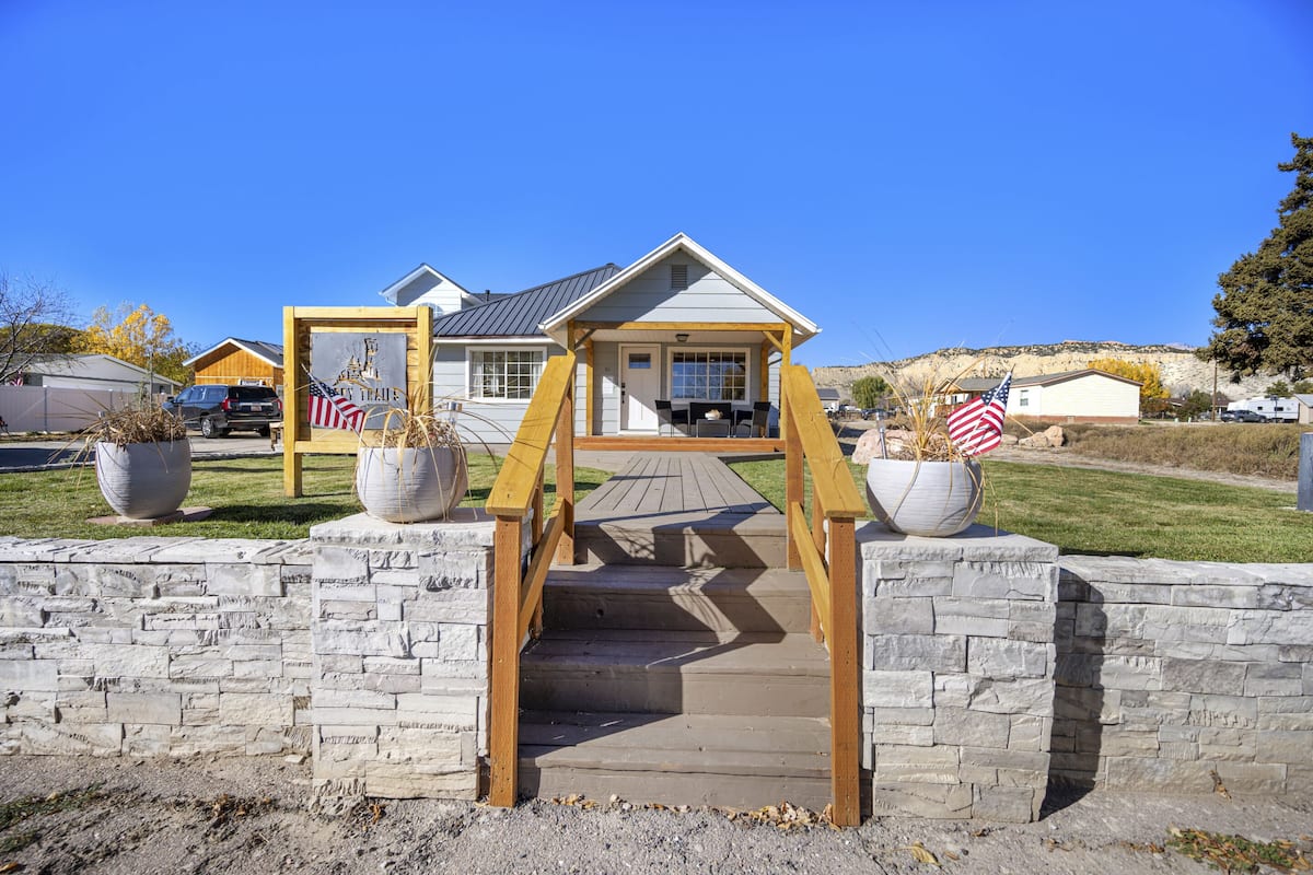 A residential property with a wooden staircase leading to a front porch, a garage, and a well-maintained lawn.