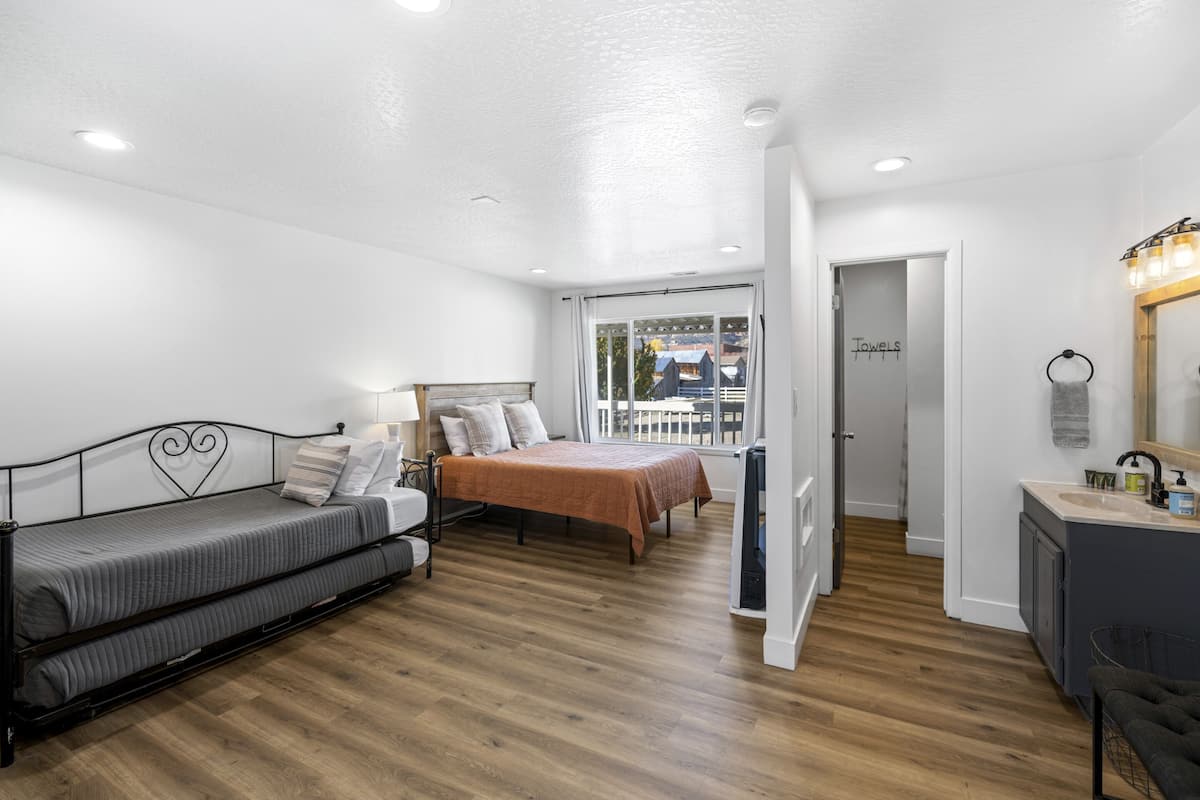 A modern bedroom with a bed, a sofa, a desk, and a bathroom with a sink and mirror.