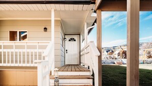 A wooden porch with a white railing, a wooden staircase leading to a white door, and a view of a construction site in the background. - Happy Trails Bed and Breakfast (Tropic)