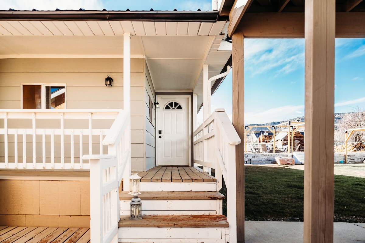 A wooden porch with a white railing, a wooden staircase leading to a white door, and a view of a construction site in the background.