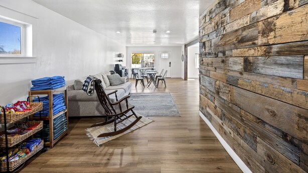 A spacious living area with a wooden wall, a sofa, a rocking chair, and a dining table with chairs. - Happy Trails Bed and Breakfast (Tropic)