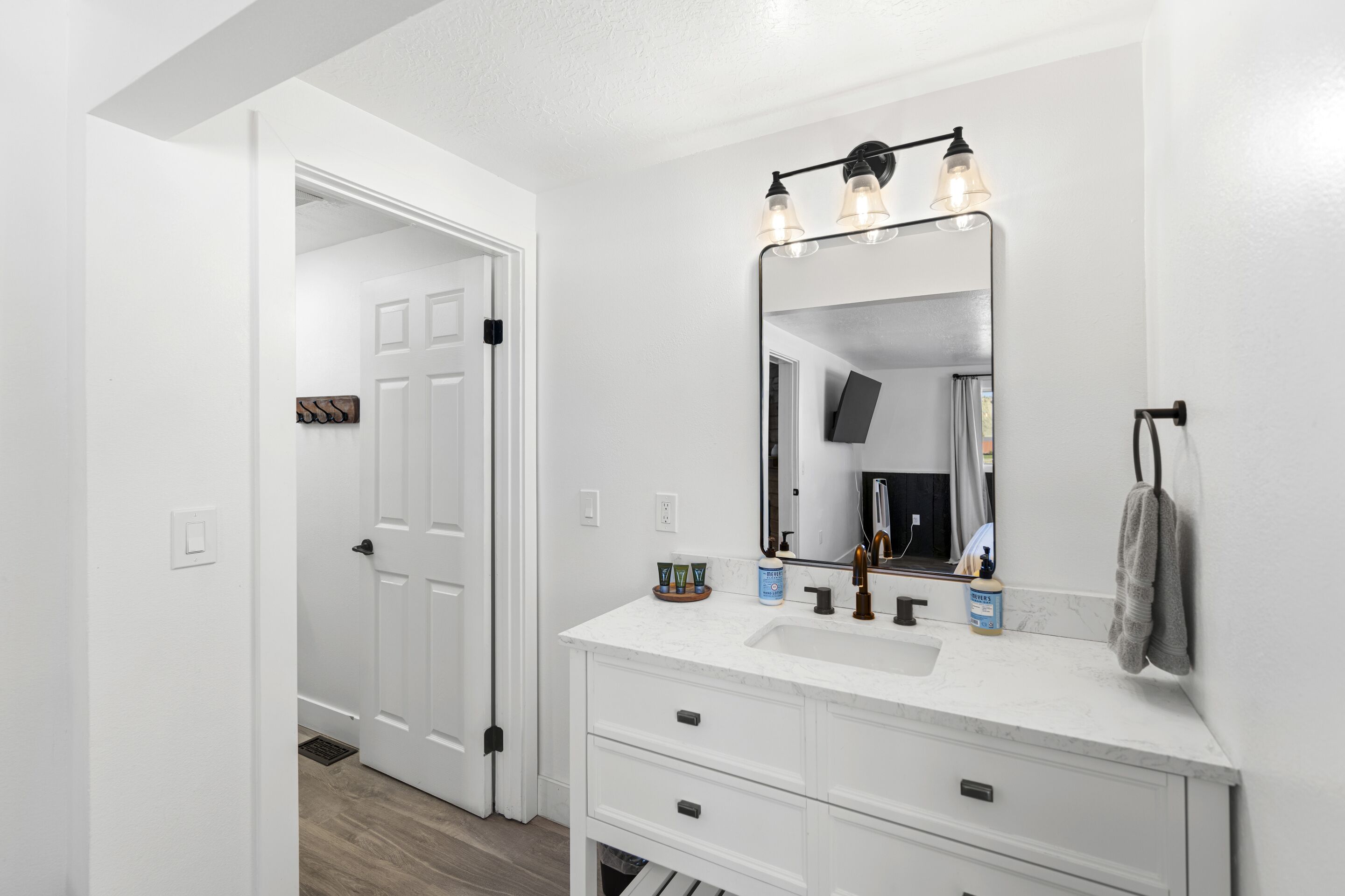 A bathroom with a white vanity, a large mirror, and a towel hanging on the wall.