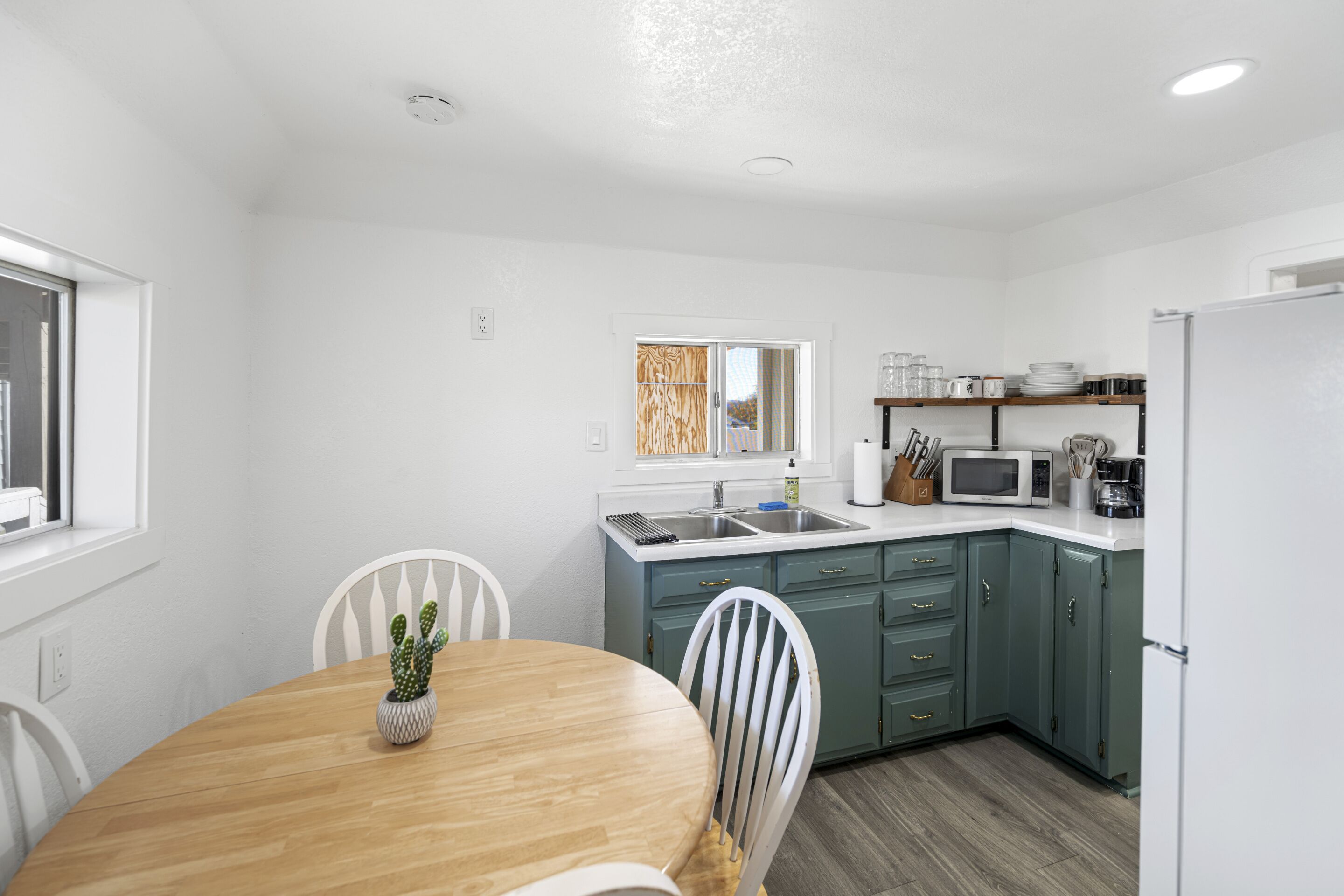 A compact kitchen with a wooden dining table, white chairs, and a built-in microwave.