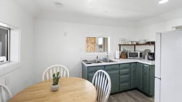 A compact kitchen with a wooden dining table, white chairs, and a built-in microwave.