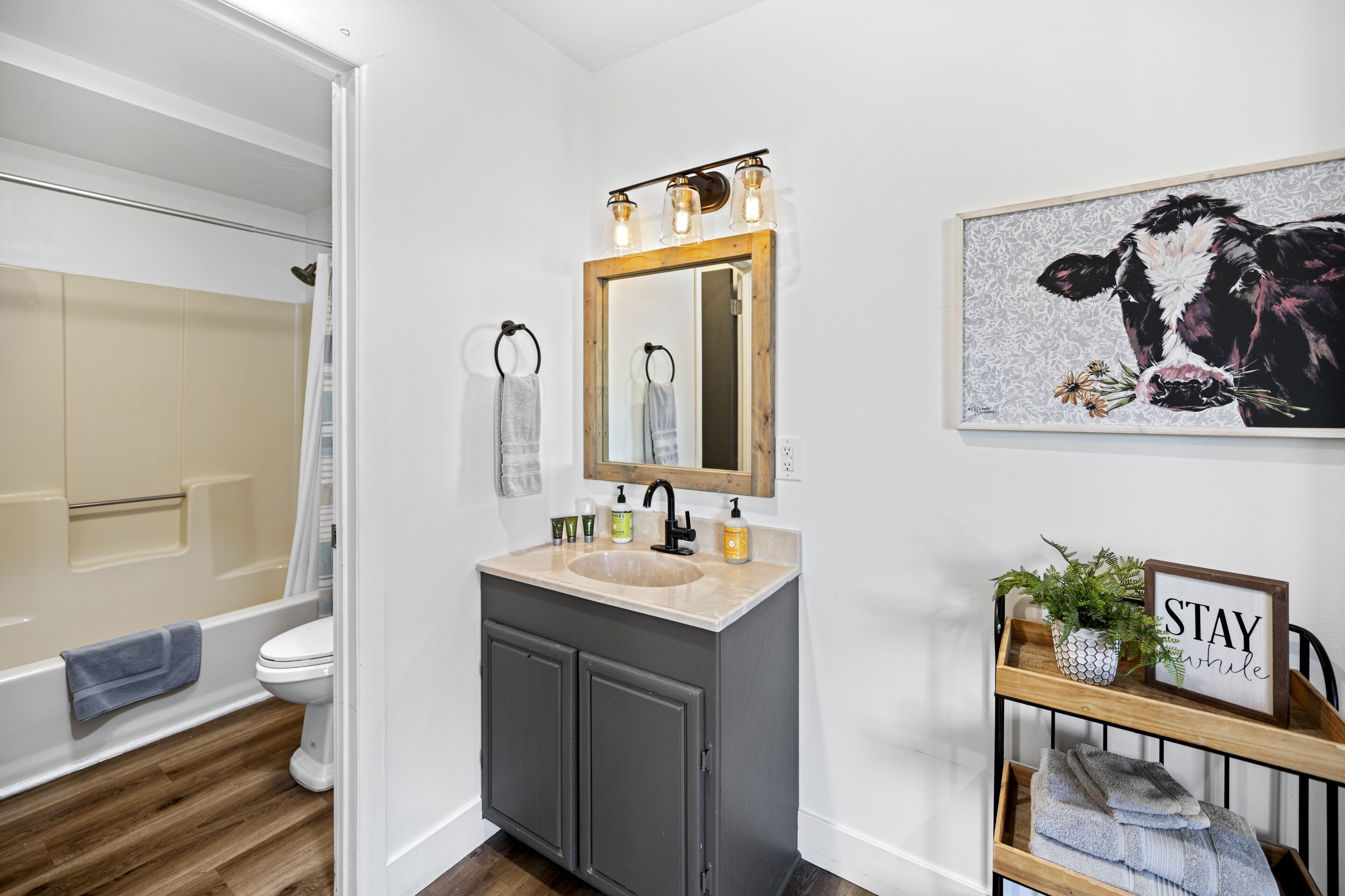 A bathroom with a wooden vanity, a mirror with lights, a toilet, and a shower area.