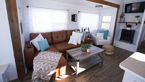 A cozy living room with a brown leather sofa, white and blue cushions, a wooden coffee table, and a fireplace. - Happy Trails Bed and Breakfast (Tropic)