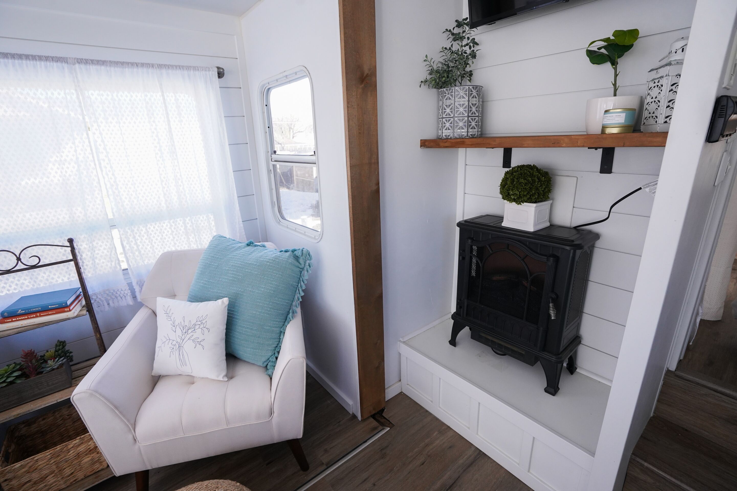 Una habitación acogedora con un sillón de cuero blanco, una estufa pequeña y una ventana con cortina translúcida.