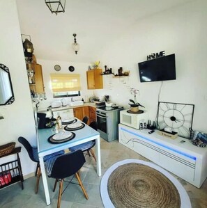 A compact kitchen with a dining area, a TV mounted on the wall, and a clock on the wall.