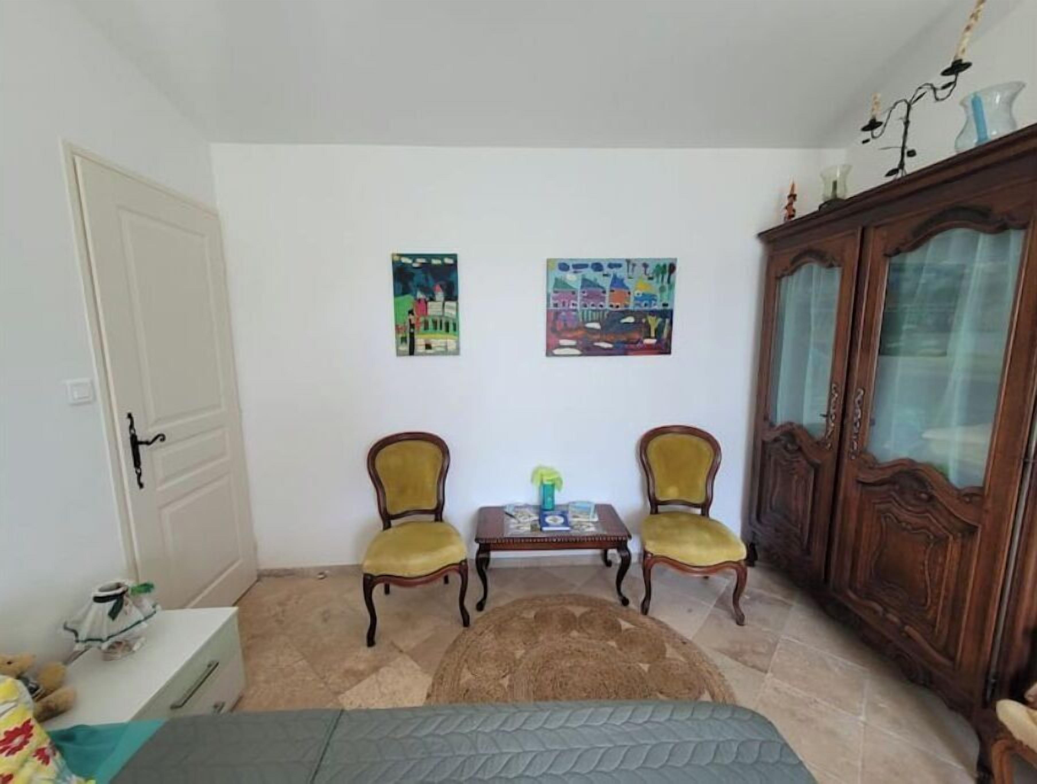 Une pièce comprenant deux fauteuils jaunes, une petite table en bois, un meuble avec des portes en verre et deux tableaux accrochés au mur.
