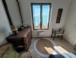 A room with a wooden dresser, a chair, a round rug, and a window with curtains.