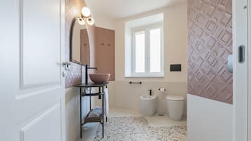 Een badkamer met een witte deur, een wastafel, een spiegel, een raam en een behang met een patroon.