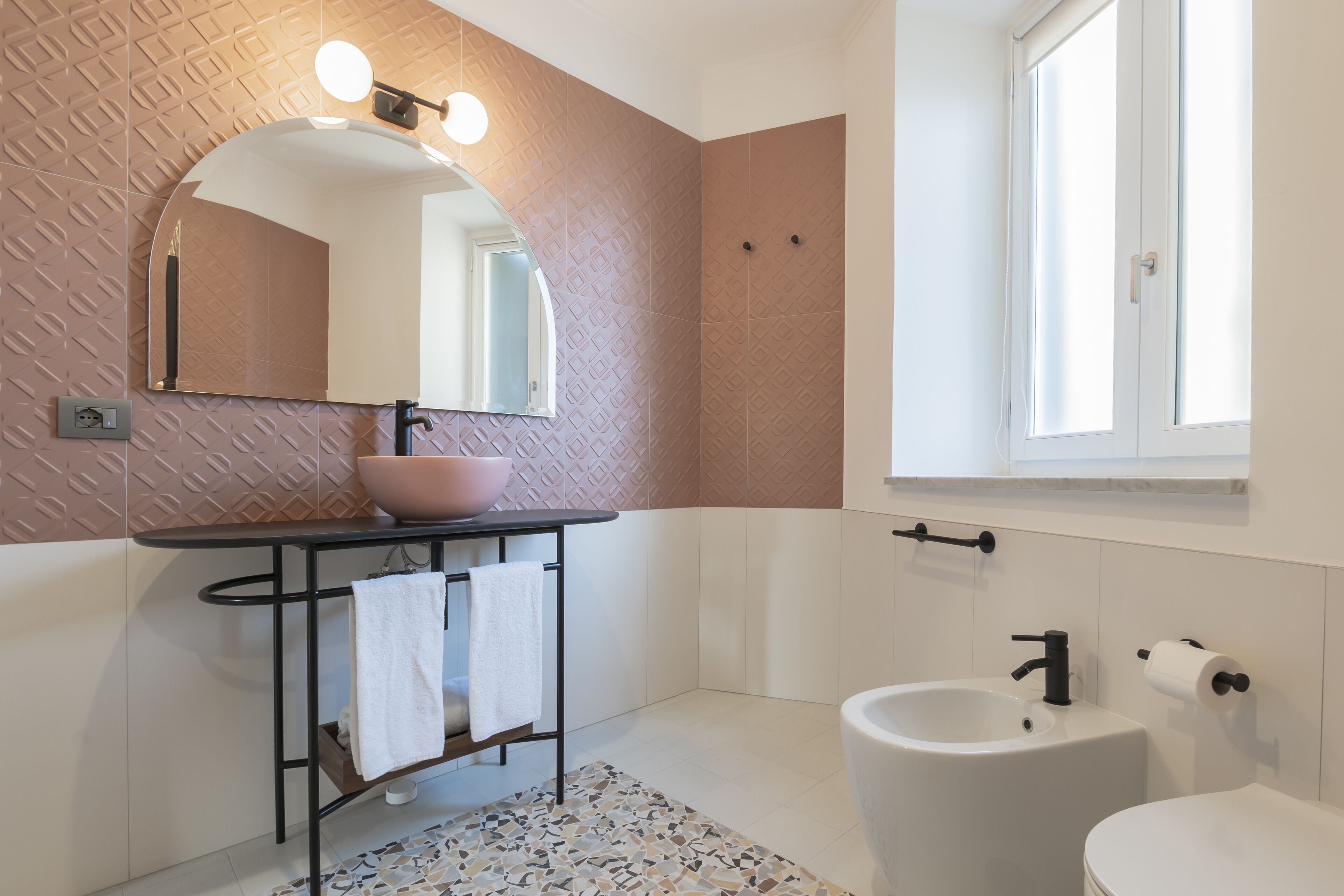 Un baño moderno con un espejo redondo, un lavabo con recipiente, un inodoro y una ventana.