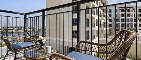 A balcony with wicker furniture and a glass table, overlooking a cityscape.