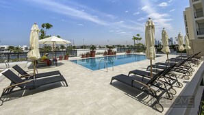 A rooftop pool area with lounge chairs and umbrellas, a clear blue sky, and a cityscape in the background. - WelHome - Incredible Waterfront Apt With Mesmerizing views (Dubai)