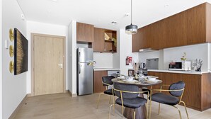 A modern kitchen with wooden cabinets, a stainless steel refrigerator, and a dining area with a round table and chairs. - WelHome - Incredible Waterfront Apt With Mesmerizing views (Dubai)