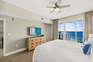 Et hotelværelse med en stor seng, et fjernsyn, en trækommode og en balkon med udsigt over havet.