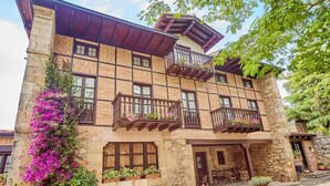 Un edificio de varios pisos de piedra con balcones de madera, ventanas amplias y plantas en macetas.