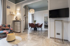 A modern living room with a sofa, a dining table with chairs, a TV mounted on the wall, and a lamp on a side table. - Be Mate Trastevere III (Rome)