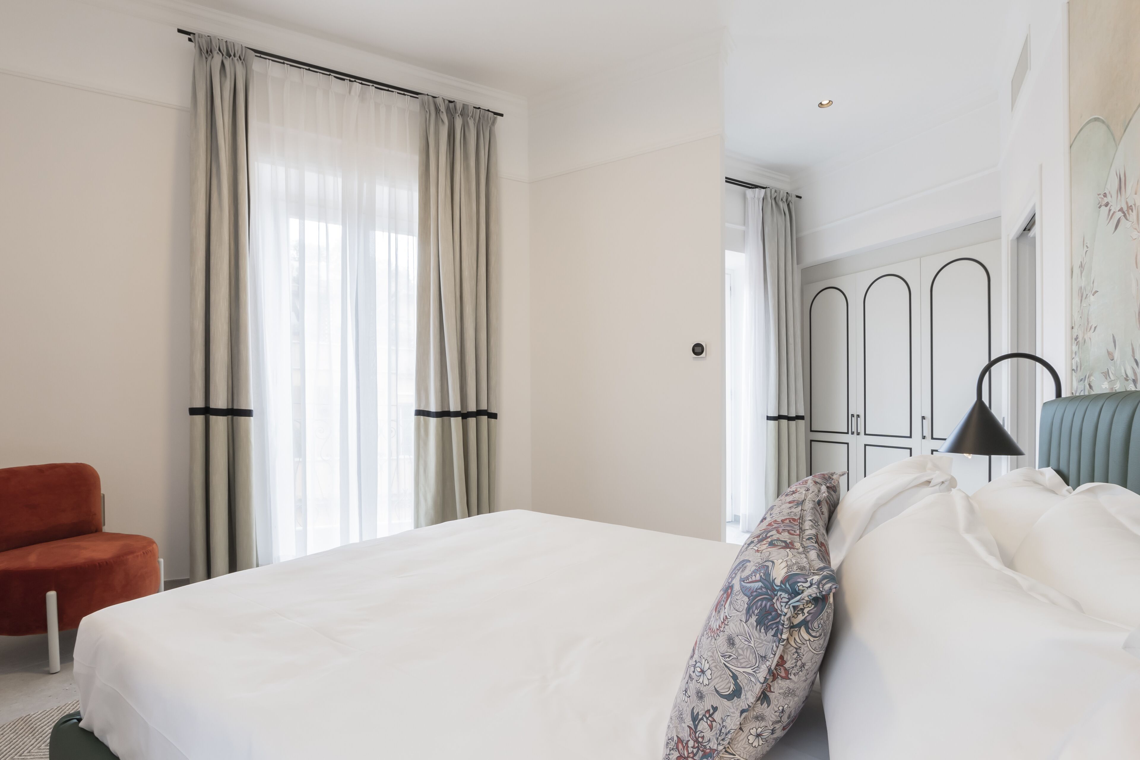 Hotellihuone, jossa on suuri sänky, tuoli ja peilillä varustettu vaatekaappi.